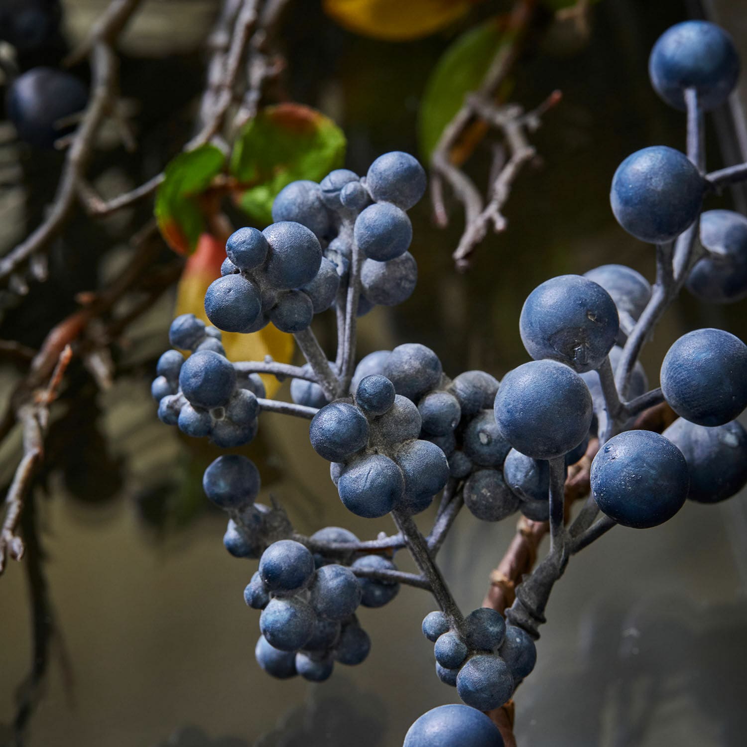 Zweig mit matten blauen Dekobeeren vor unscharfem, natürlichem Hintergrund