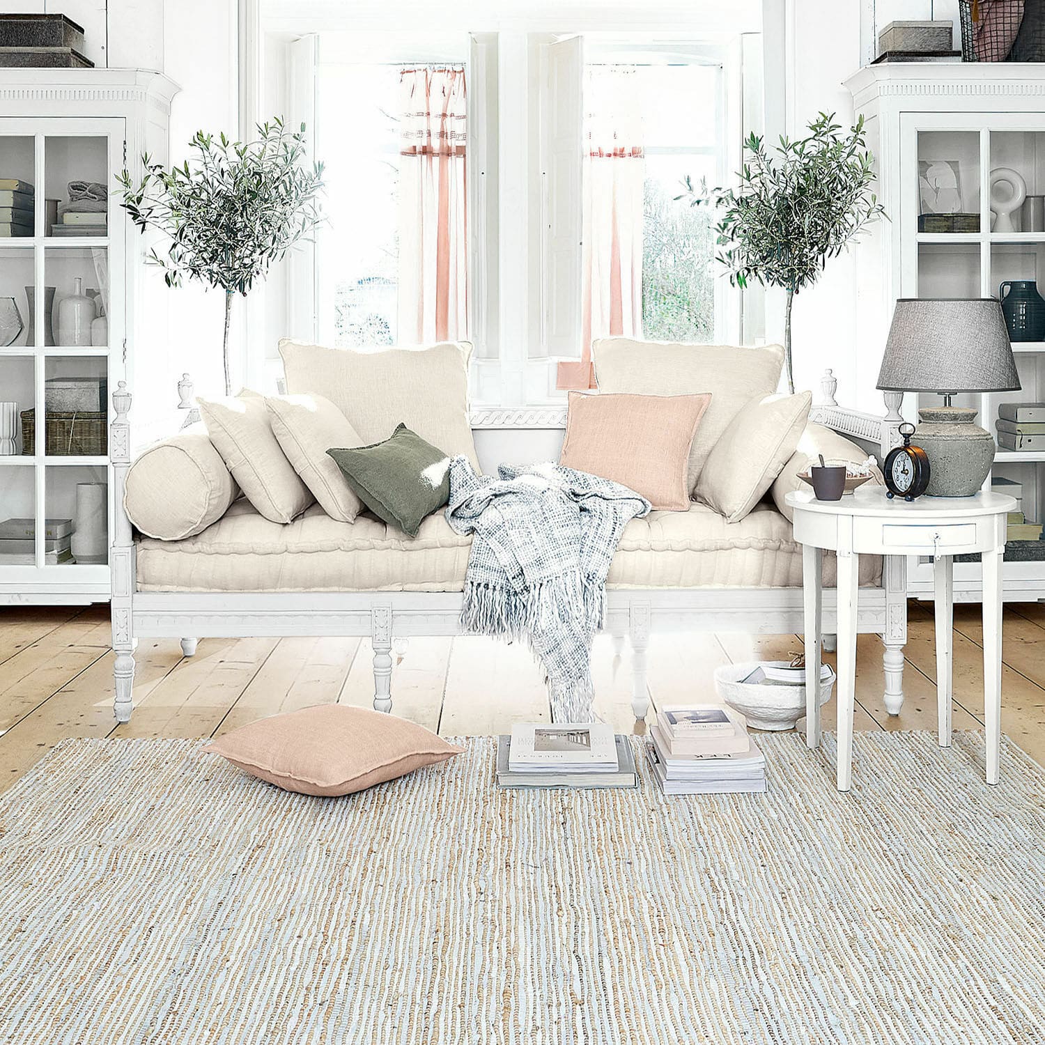 Helles Sofa mit beigen Kissen und Plaid in gemütlichem, lichtdurchflutetem Wohnzimmer mit Holzboden
