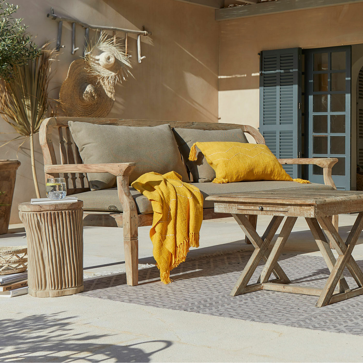 Holzsofa mit grauen Kissen und gelber Decke auf Terrasse mit Holztisch und Dekorationen