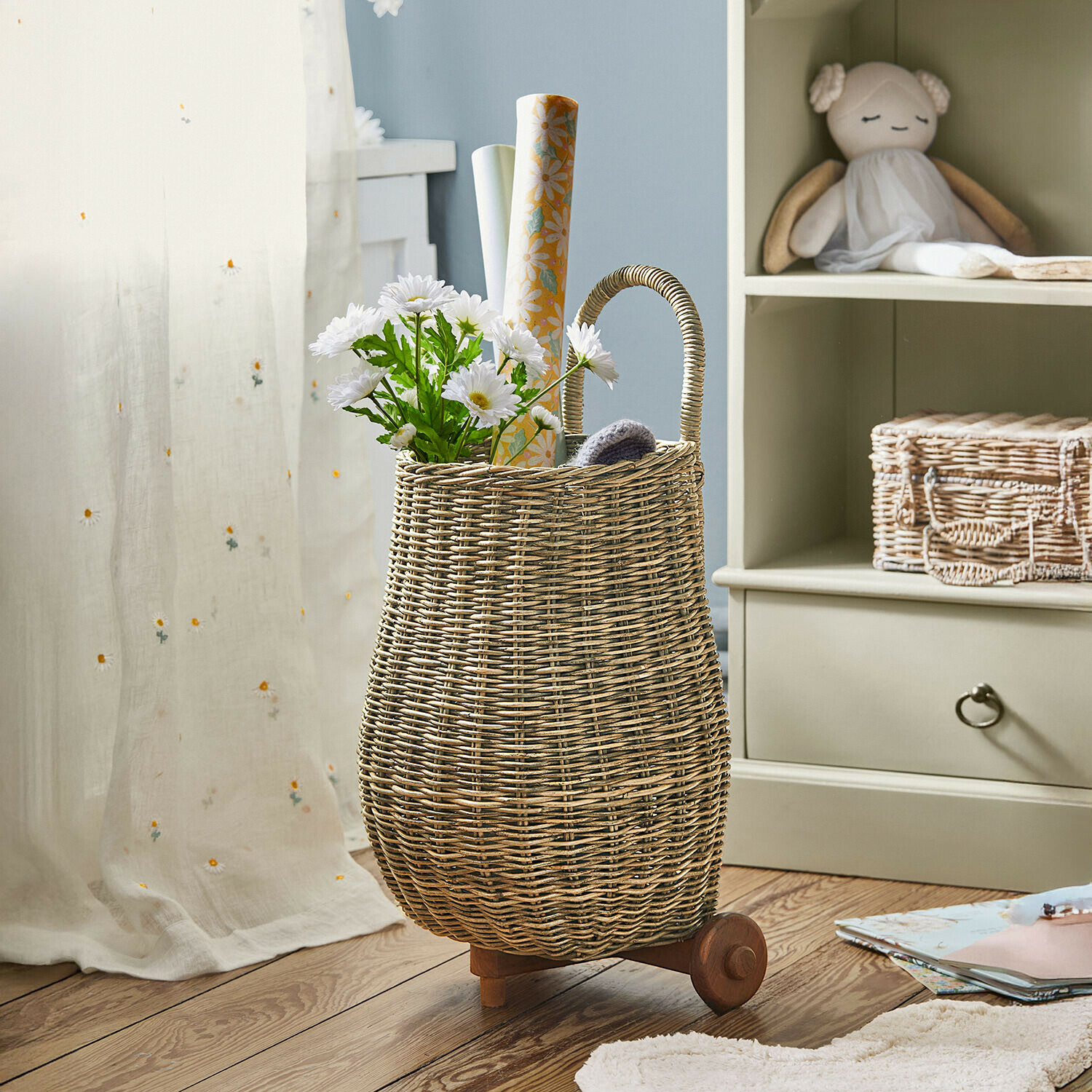 Kindertrolley Tinytreasure Natürlicher Weidenkorb auf Rollen mit Griff, gefüllt mit weißen Blumen und Dekorpapier