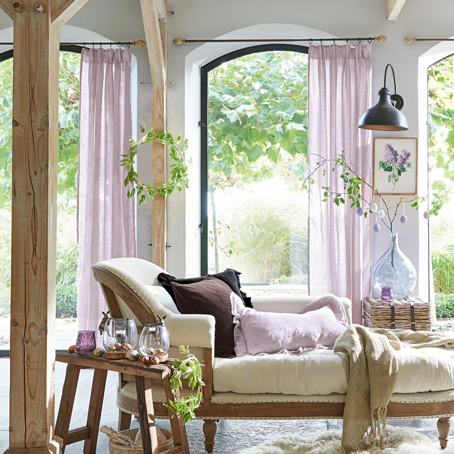 Bequeme beige Chaiselongue mit pastellfarbenen Kissen in hellem Raum mit rosa Vorhängen und natürlicher Dekoration