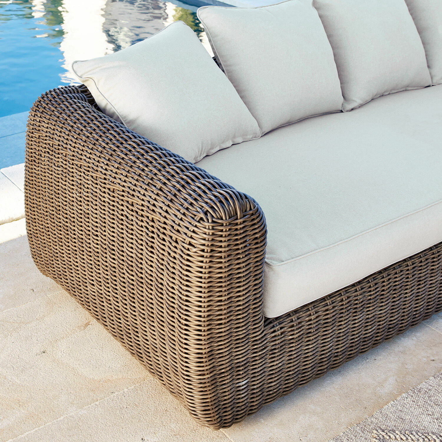 Gartensofa aus braunem Rattan mit hellbeigen Kissen, ideal für Terrasse am Pool
