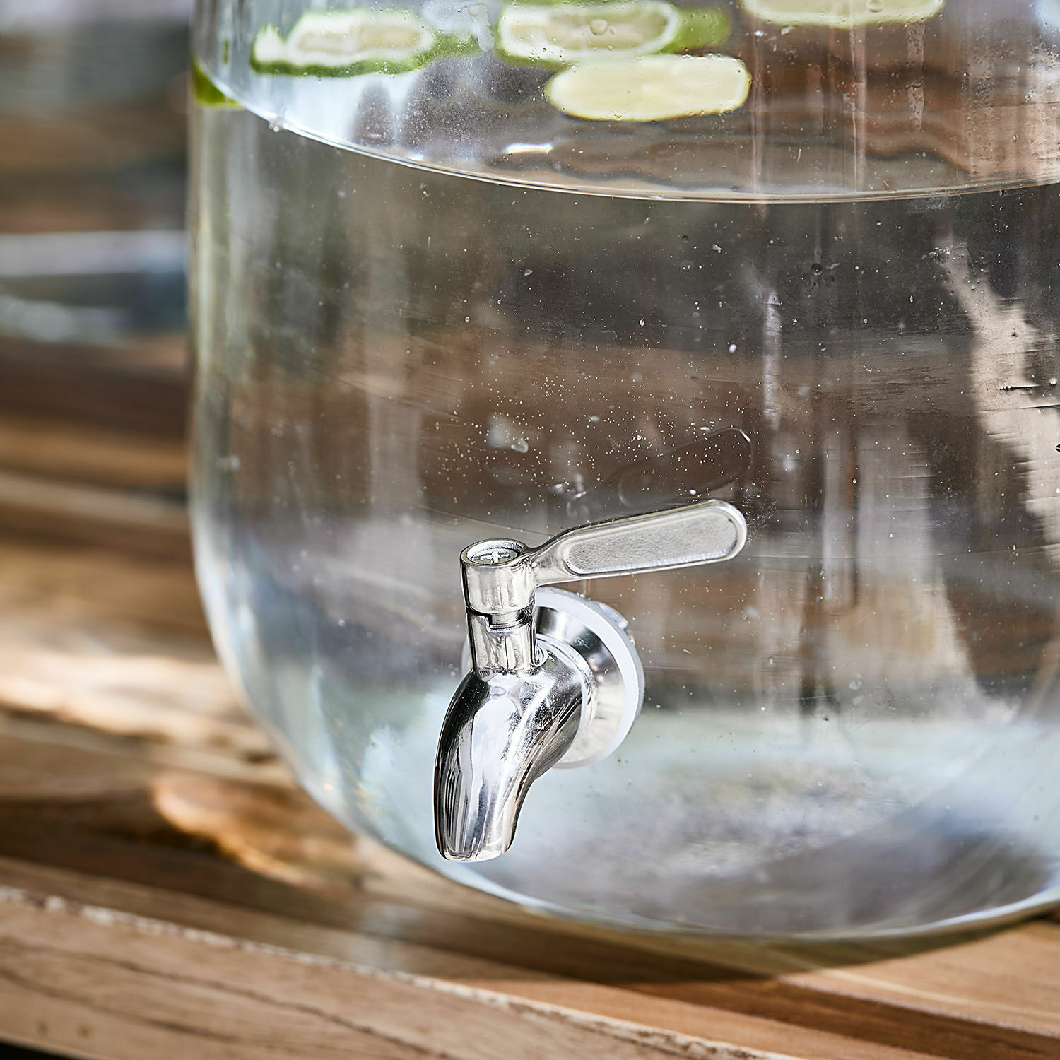 Glasbehälter mit Metallauslauf und Limettenscheiben, ideal zum Servieren von Wasser oder Getränken.