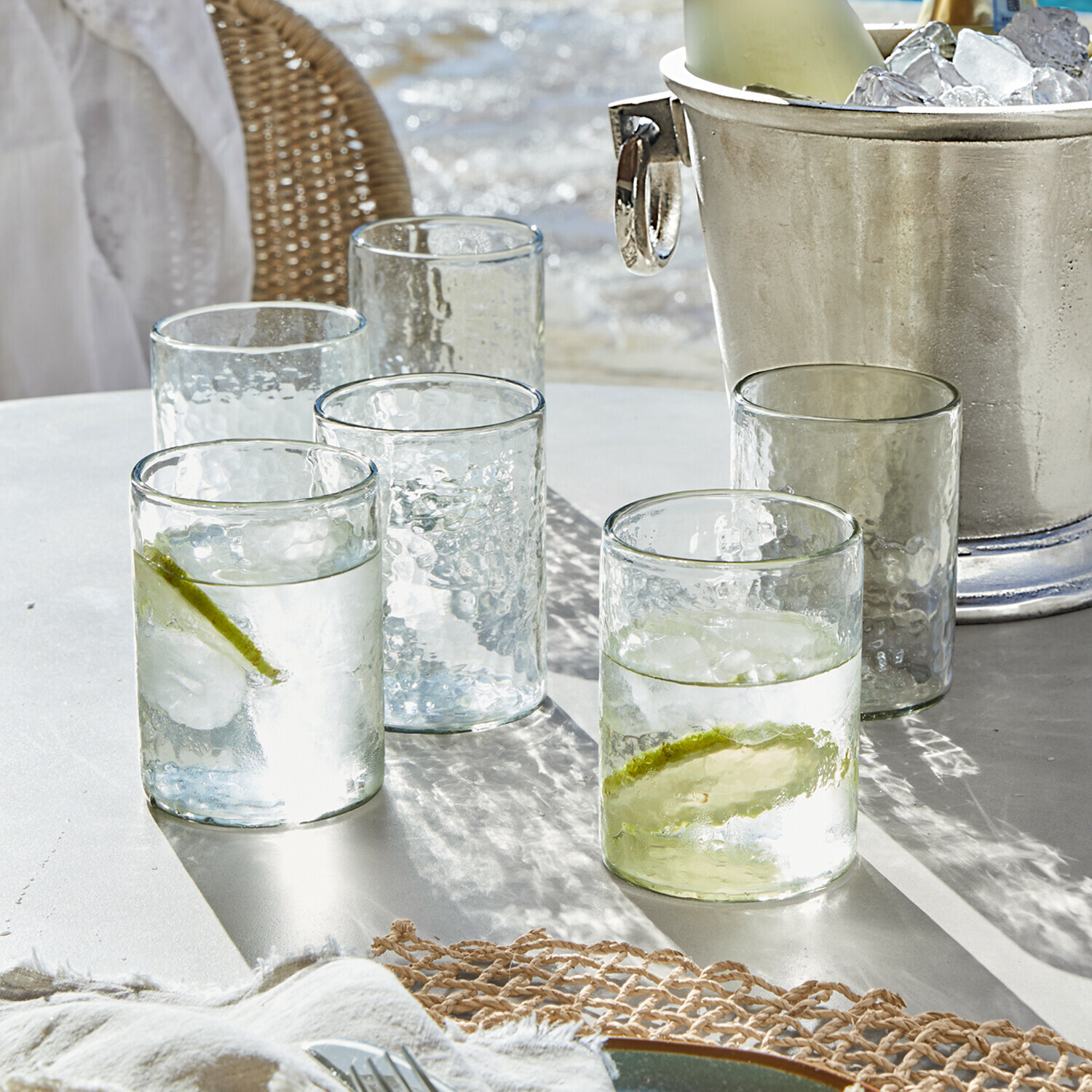 Gläser aus klarem, strukturiertem Glas mit Limettenscheiben und Eiswürfeln auf weißem Tisch