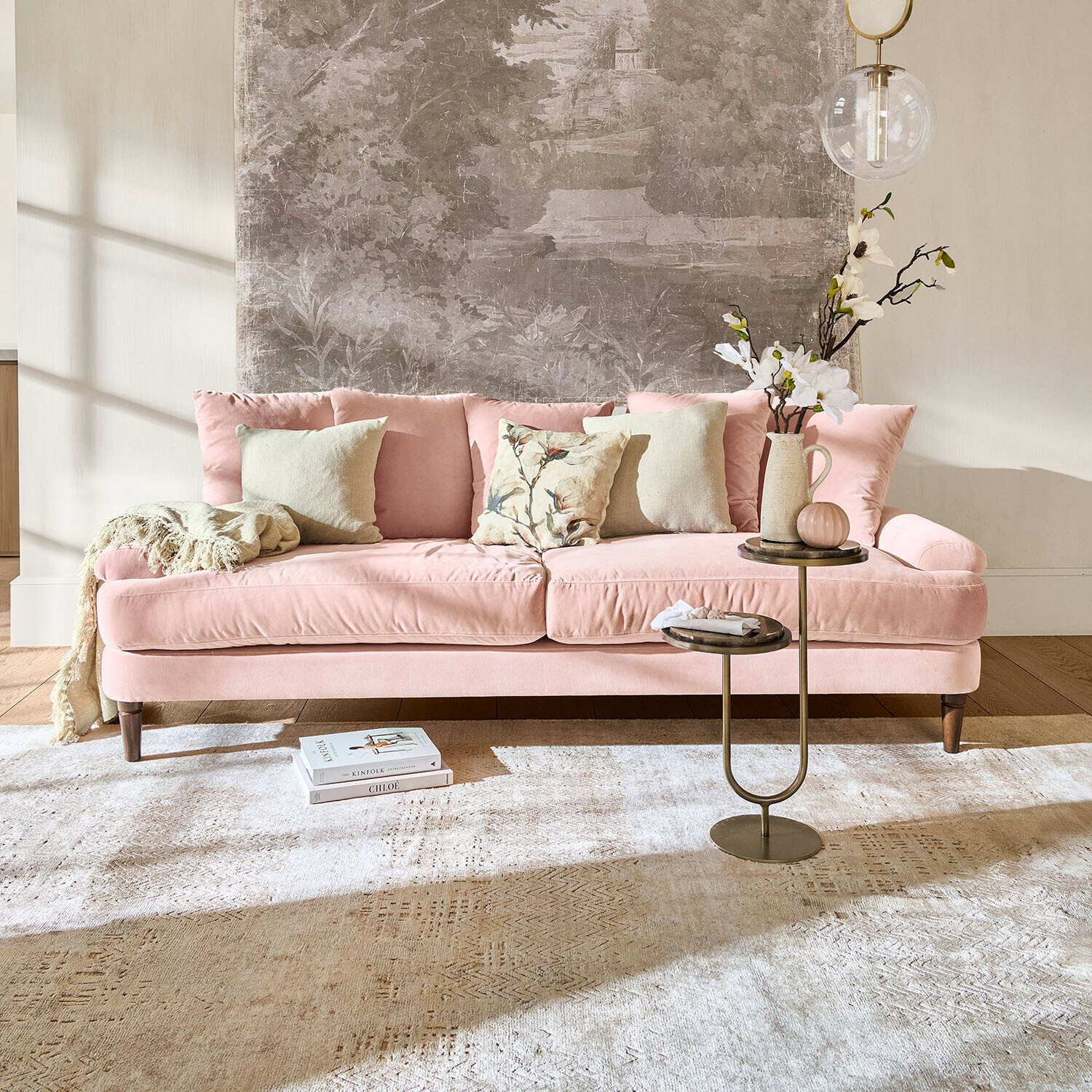 Sofa Rivermere Rosa Samtsofa mit Kissen und Beistelltisch in hellem Wohnzimmer mit Wanddekoration
