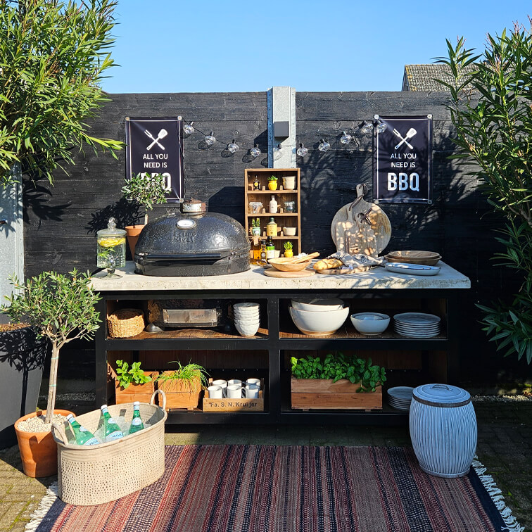 Outdoor-Grillstation mit schwarzem Grill, weißer Arbeitsplatte, Pflanzen und Küchenutensilien