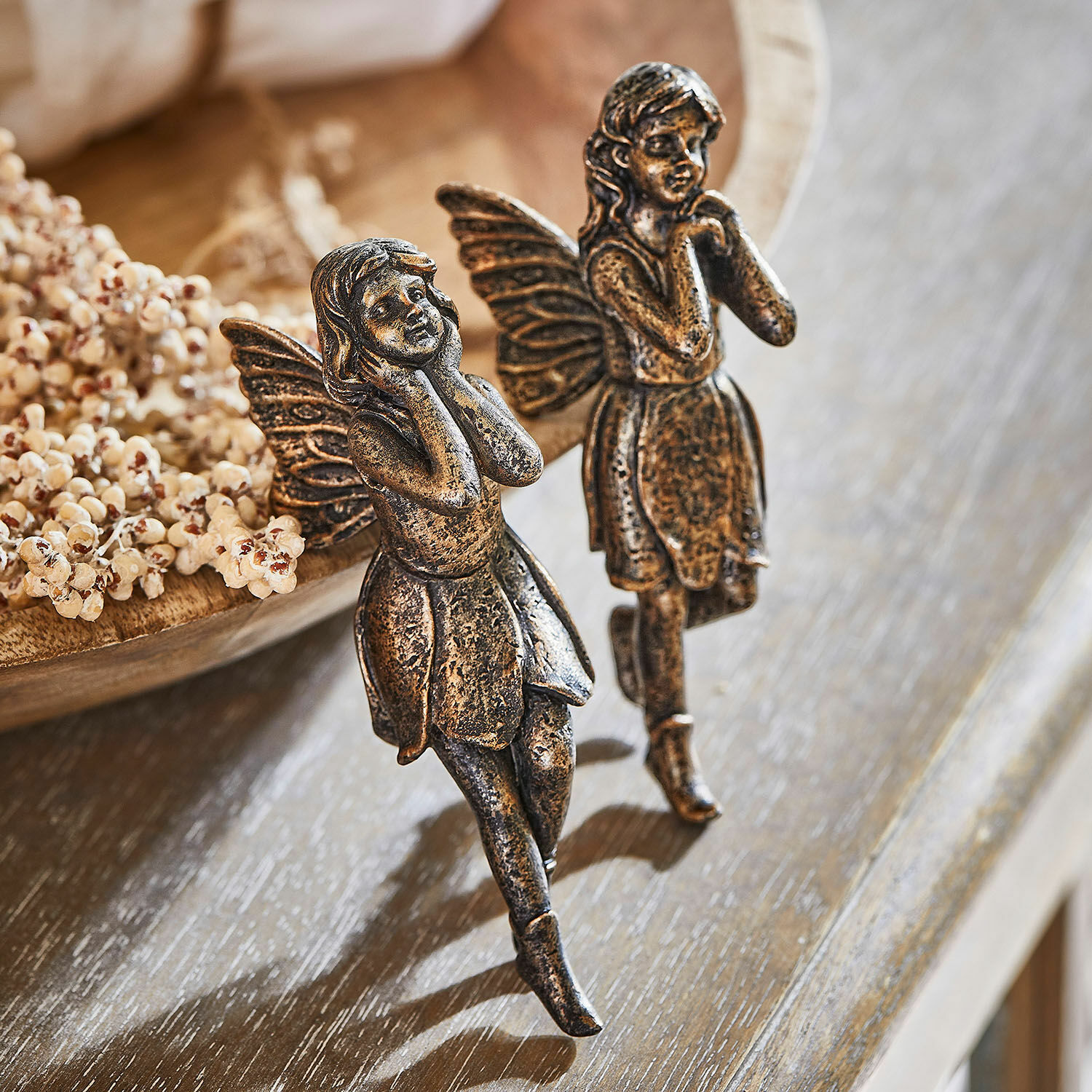 Zwei dekorative Feenfiguren aus Metall in Altgold auf Holztisch, stilvolle Wohnaccessoires