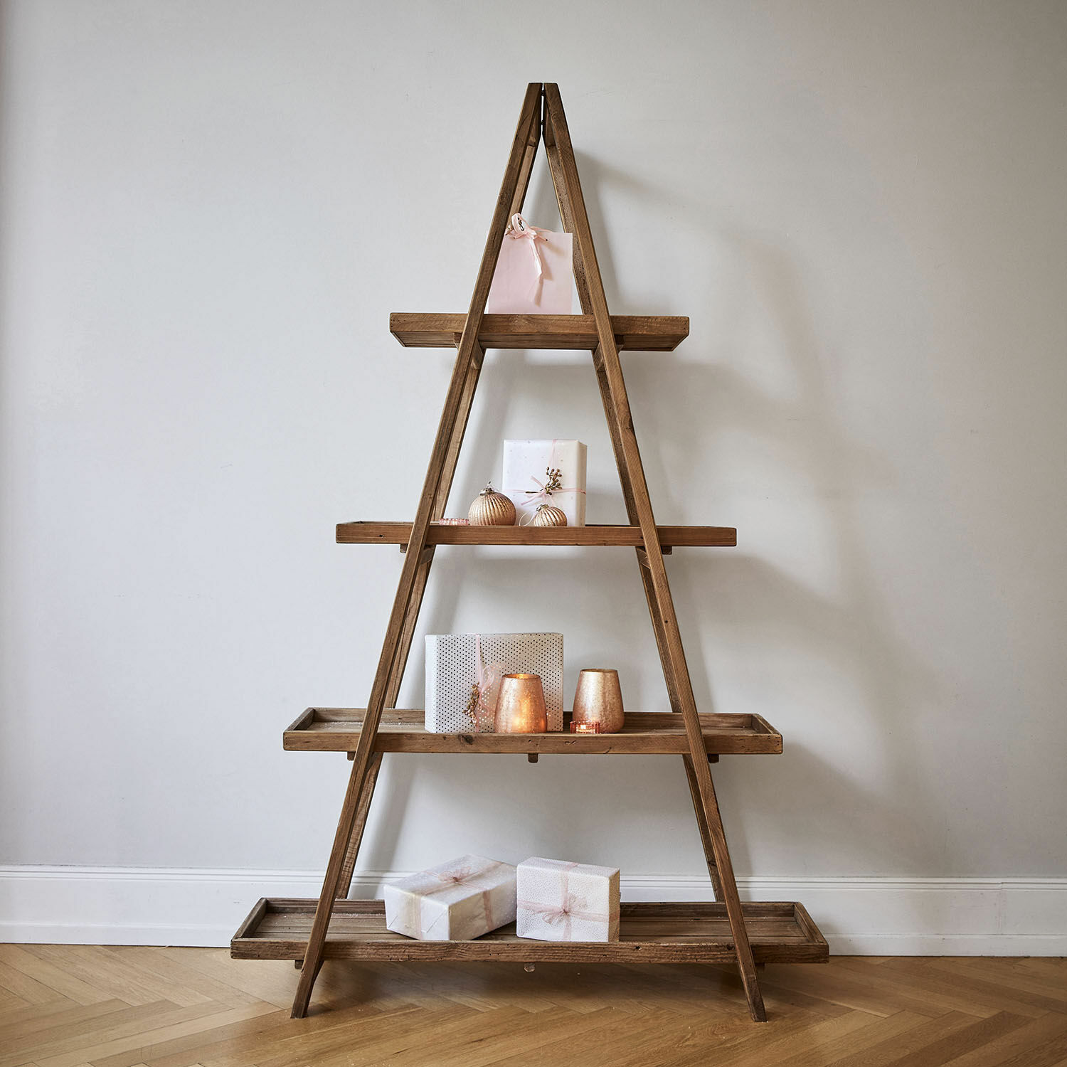 Holzregal in A-Form mit pastellfarbenen Dekorationen und Geschenken auf hellem Parkettboden.