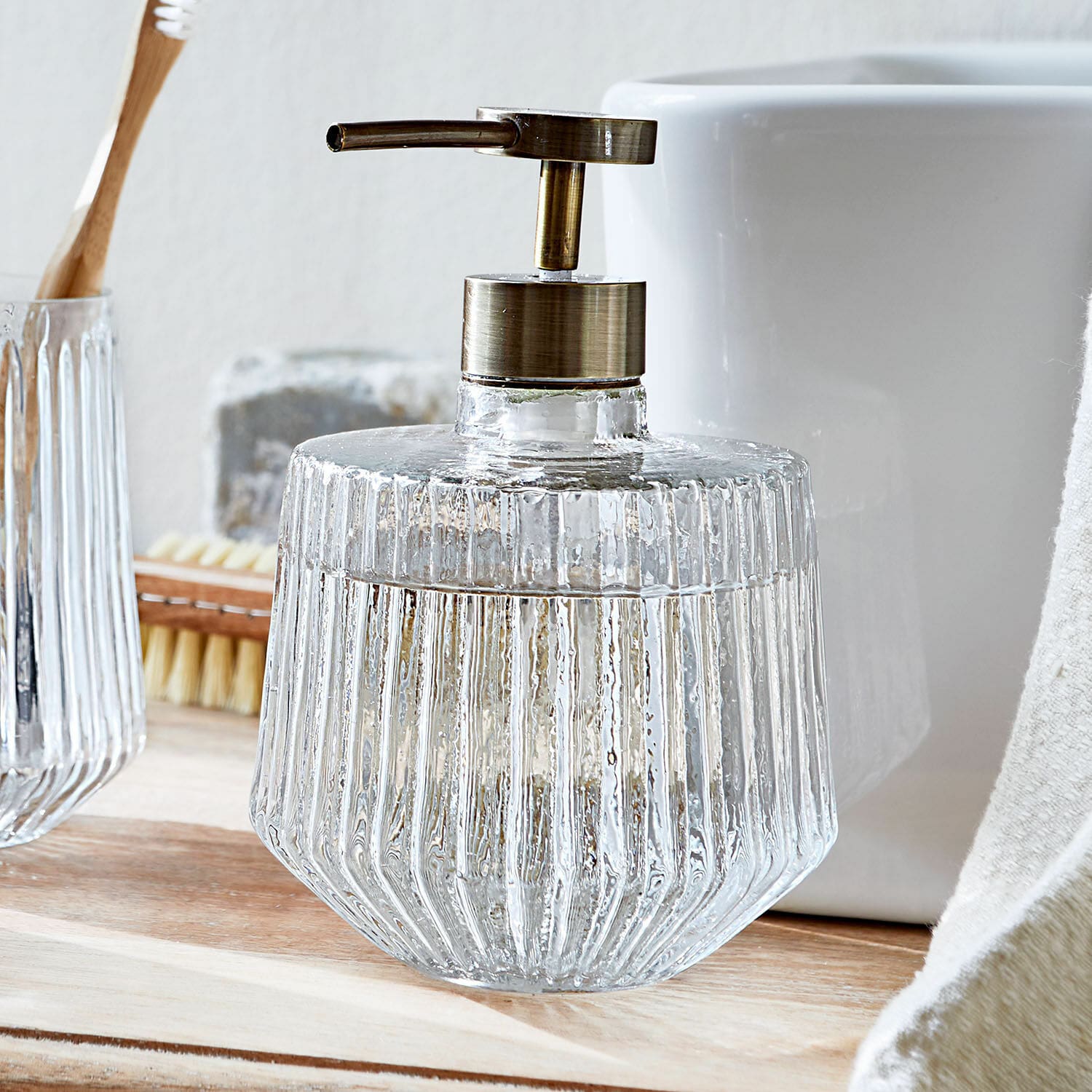 Transparenter Glas-Seifenspender mit Metallpumpe in Messingoptik auf Badezimmerablage