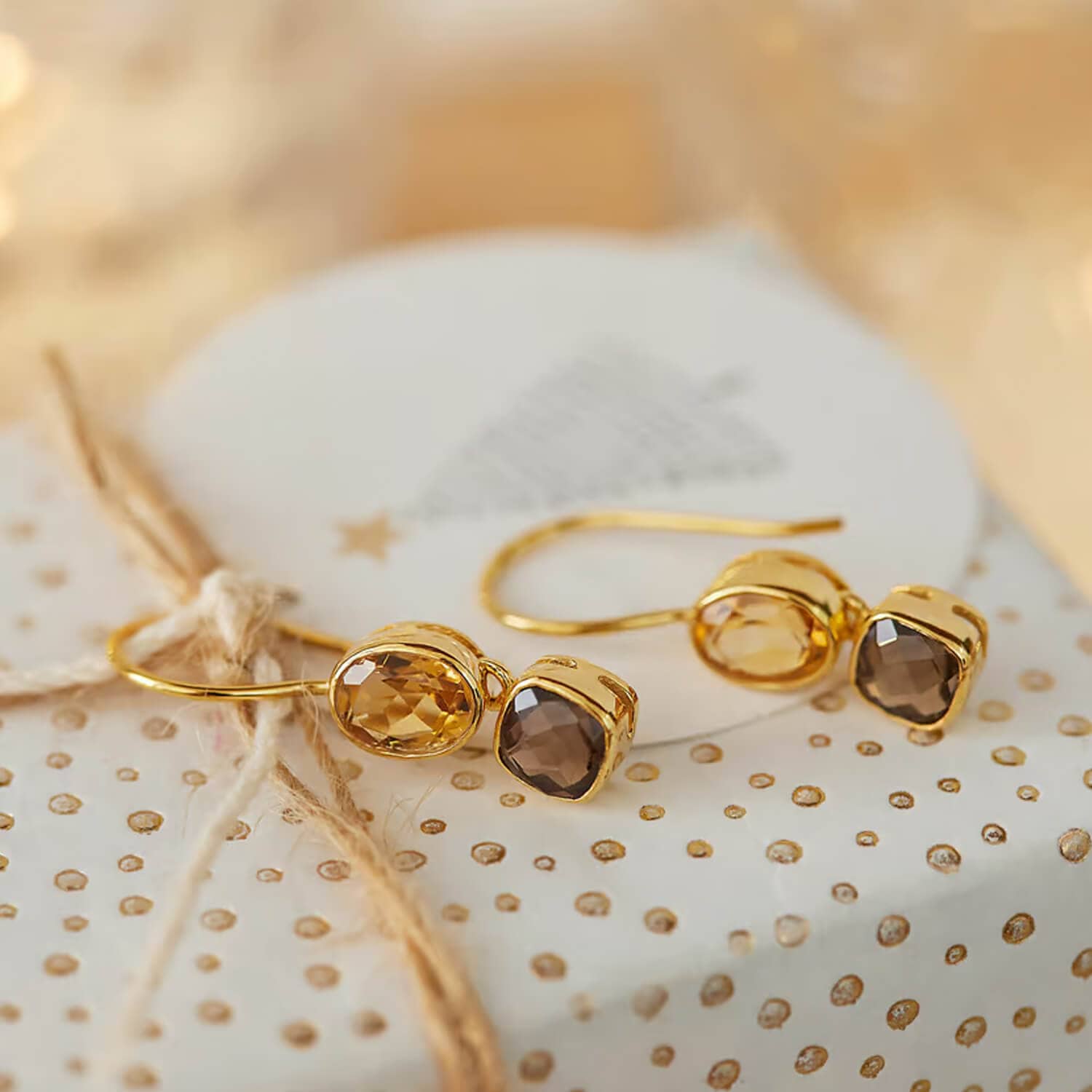 Goldene Ohrringe mit zwei facettierten Steinen in Bernstein- und Brauntönen auf dekorativem Papier