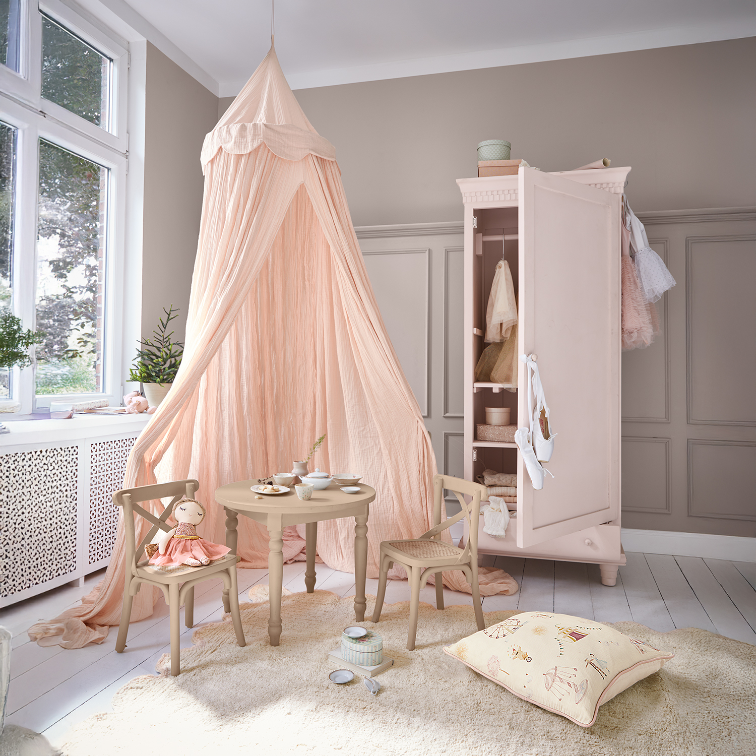Gemütliches Kinderzimmer mit rosa Baldachin, rundem Holztisch, Stühlen und offener rosa Garderobe