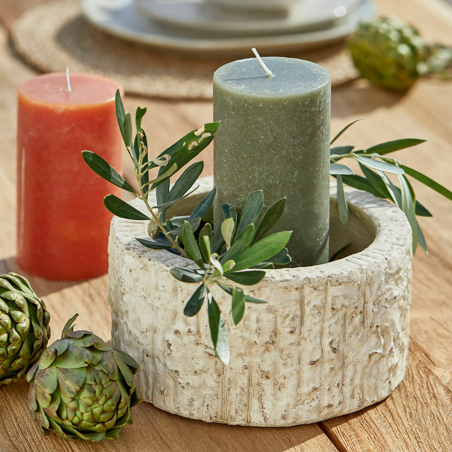 Runder Kerzenhalter aus beigem Stein mit grüner Kerze und Blattdeko auf Holztisch
