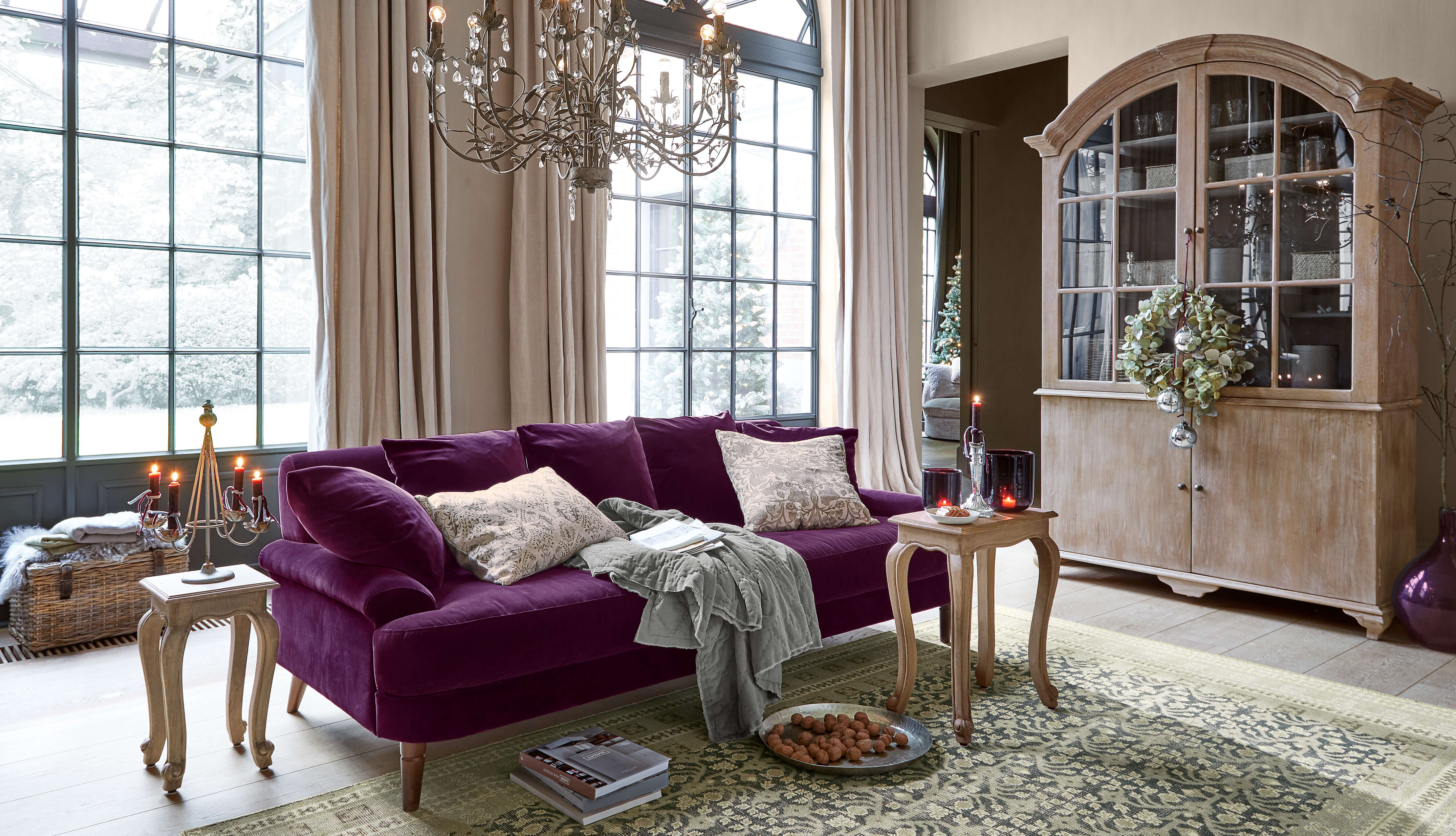 Violette Samtsofa mit beigen Kissen und Holztischen in hellem Wohnzimmer