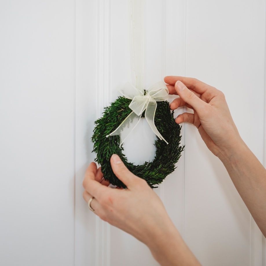 Kleiner grüner Weihnachtskranz mit weißer Schleife an weißer Tür, festliche Dekoration