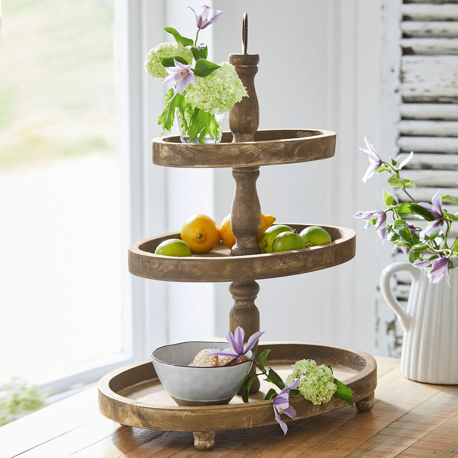 Etagere Olathe Dreistöckiges Holz-Etagere mit Früchten und Blumen auf Holztisch in hellem Raum