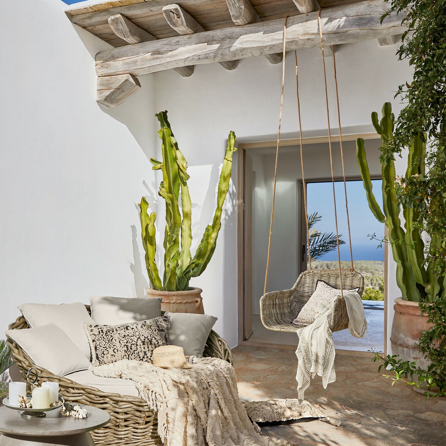 Gemütliche Terrasse mit Rattansofa und Rattanschaukel in Naturtönen, Dekorationen und Kakteen