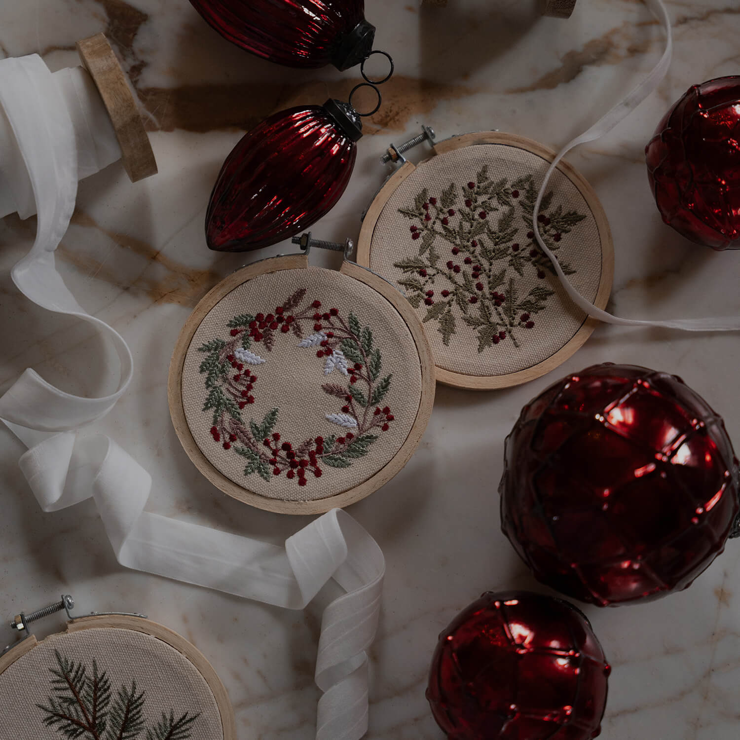Weihnachtsschmuck mit bestickten Pflanzenmotiven auf beigem Stoff und roten Christbaumkugeln