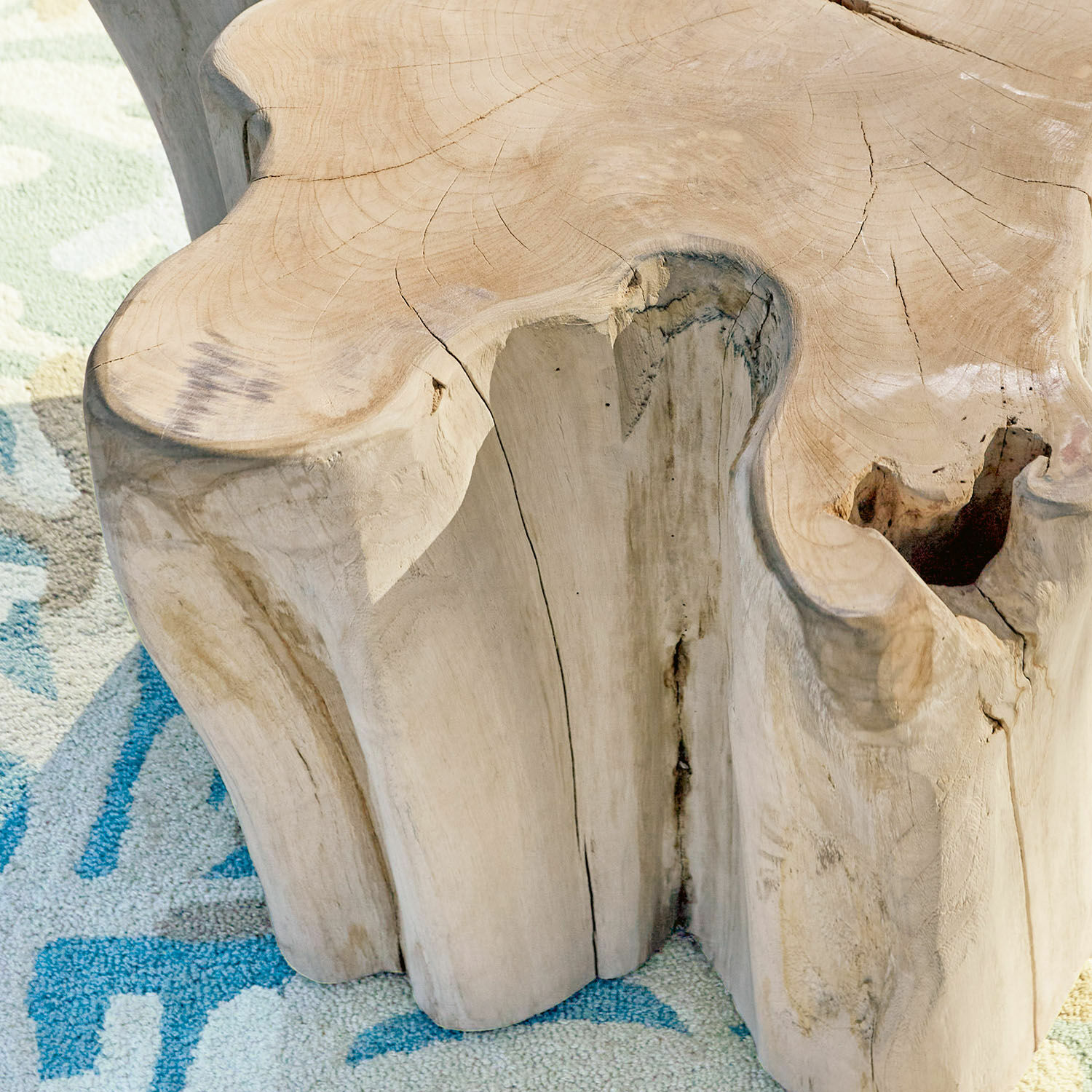 Natürlicher Couchtisch aus massivem Holz mit unregelmäßiger Form auf blau gemustertem Teppich