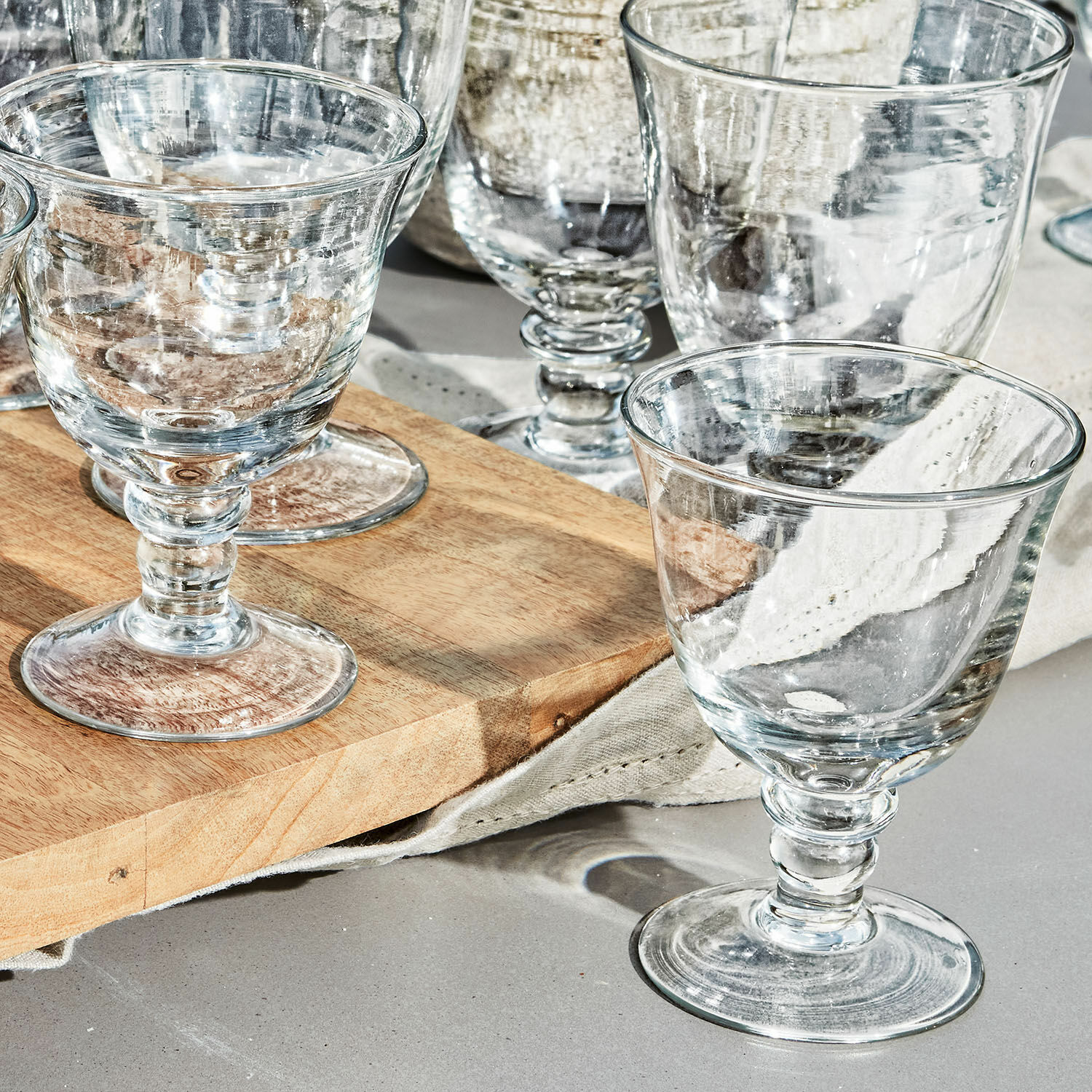 Set aus transparenten Gläsern aus Glas mit Stiel auf einem Holzbrett zum Servieren