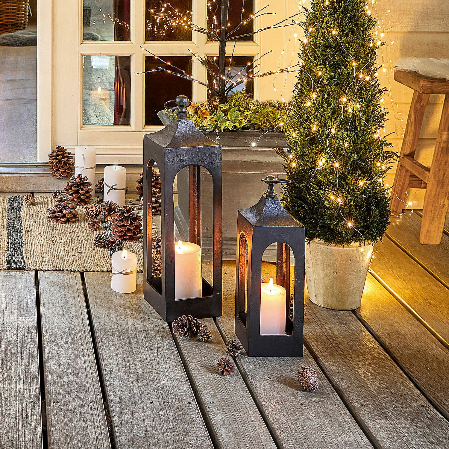 Zwei schwarze Metalllaternen mit weißen Kerzen auf Holzterrasse mit weihnachtlicher Dekoration