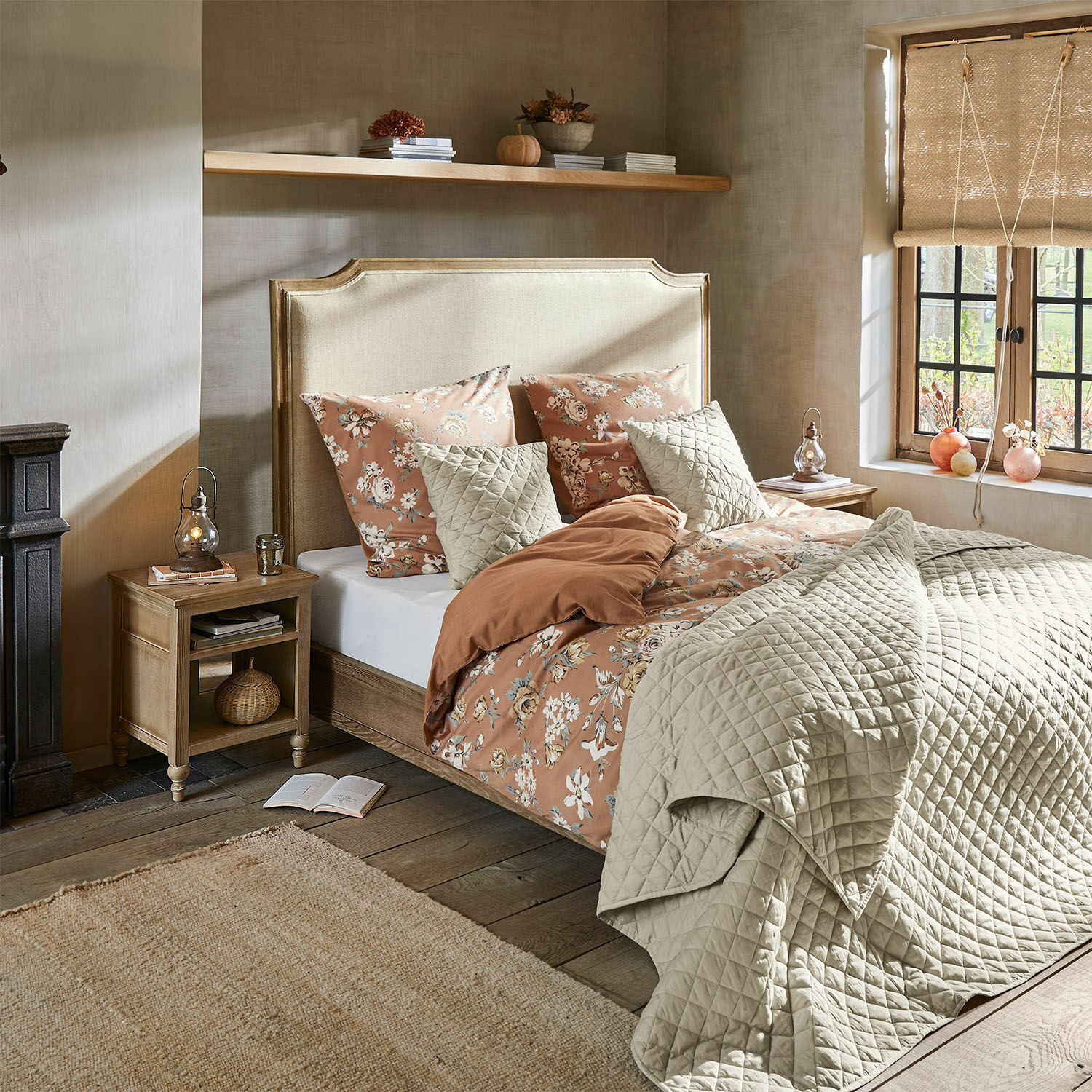 Schlafzimmer mit beige gepolstertem Kopfteil, floraler Bettwäsche und hellbeiger Steppdecke