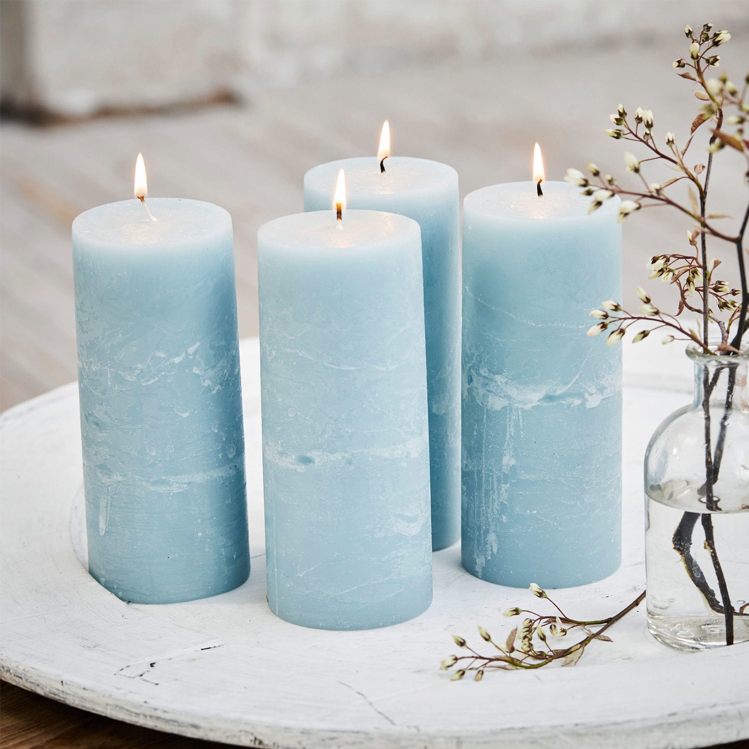 Kerze 4er Set Homel Vier blaue Wachskerzen auf weißem Dekotablett mit Zweig und Blütenarrangement