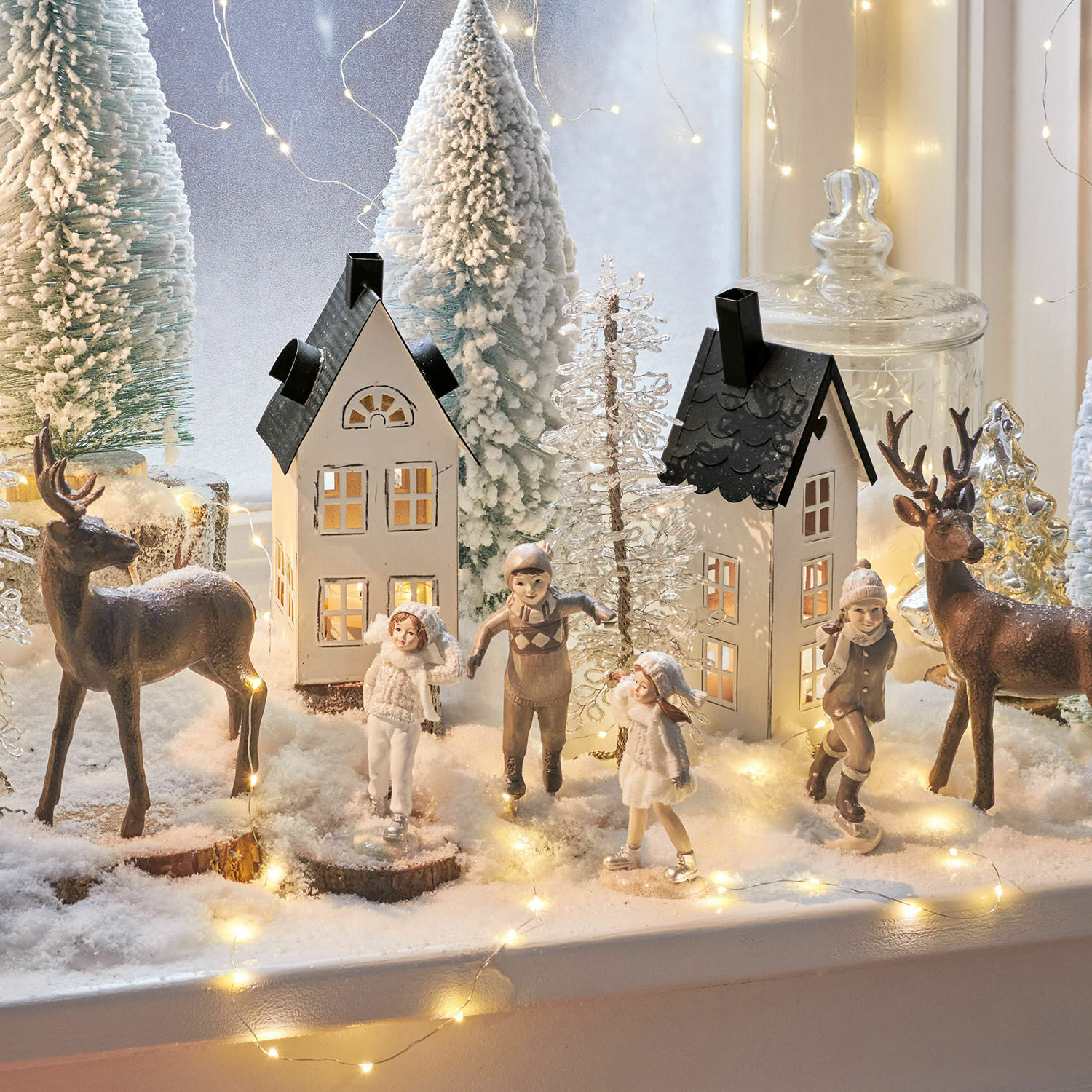 Winterliche Dekoration mit Kinderfiguren, Rentieren und Häusern im Schnee mit LED-Lichterkette