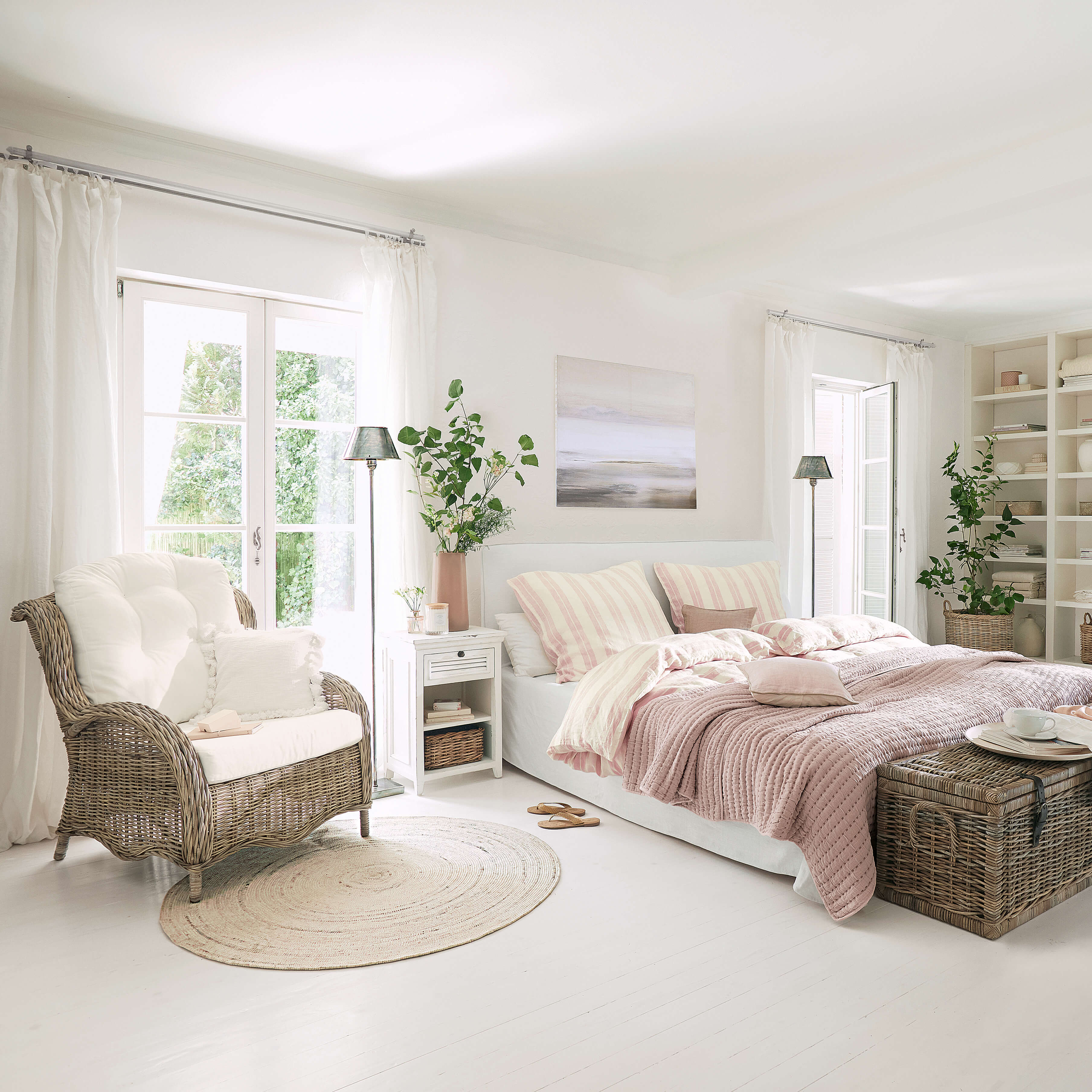 Helles Schlafzimmer mit weißem Bett, rosa Bettwäsche und Korbsessel auf hellem Boden